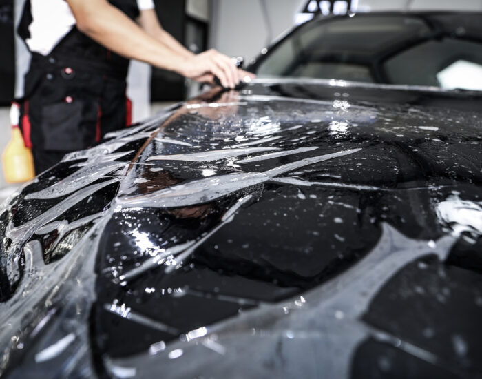 Close up of paint protection film installation on front bumper of modern luxury car. PPF is polyurethane film applied to car surface to protect the paint from stone chips, bug splatter, and abrasion
